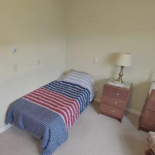 A simple bedroom with a single bed featuring striped bedding, accompanied by a nightstand and lamp.