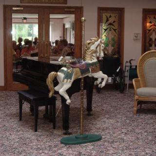 A decorative carousel horse stands beside a piano in a cozy living room setting.