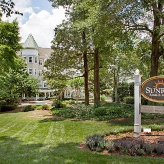 A view of a Victorian-style hotel surrounded by lush greenery and trees, with a welcoming sign at the entrance.