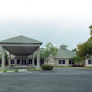 A building with a covered entrance and surrounding greenery on an overcast day.