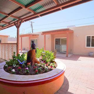 A serene courtyard featuring vibrant flowers and a decorative sculpture, surrounded by residential buildings.