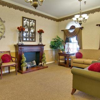 A traditionally styled living room with a fireplace, armchairs, and sofas adorned with red cushions.
