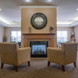 A cozy living room featuring two chairs facing a modern fireplace with a large clock above it.