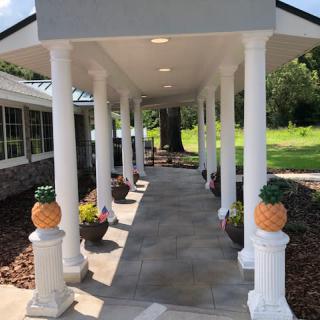 A covered walkway with white columns and decorative pineapples, leading through a landscaped garden area.