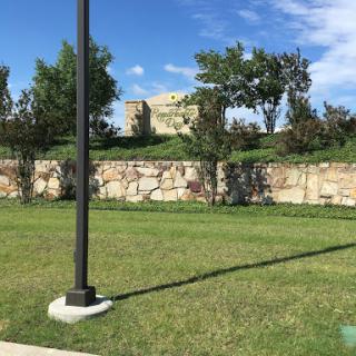 A serene park setting with a lamp post casting a shadow on the vibrant green grass.