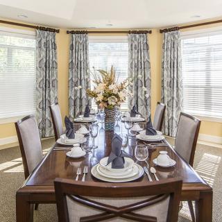 An elegantly set dining room table with a floral centerpiece and patterned curtains.