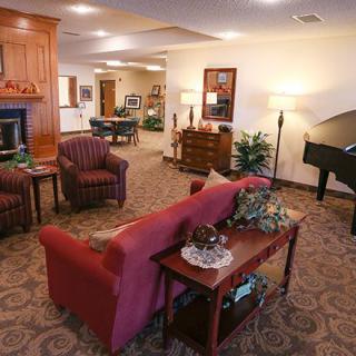 A cozy living room with warm lighting, featuring a sofa, armchairs, and a piano.