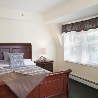A cozy bedroom with a wooden bed frame, soft lighting, and a window adorned with curtains.