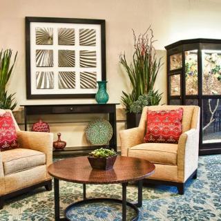 A cozy living room with two armchairs, a round coffee table, decorative plants, and framed artwork on the wall.