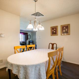 A cozy dining room with an oval table and mixed-style chairs under a hanging chandelier, adorned with framed artwork on the walls.
