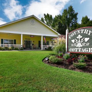 A charming yellow cottage with a welcoming sign, surrounded by lush greenery.