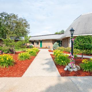 A beautifully landscaped pathway leading to a brick building, adorned with colorful flowers and greenery.