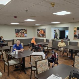 A group of elderly people sitting in a dining hall, engaging in conversation.