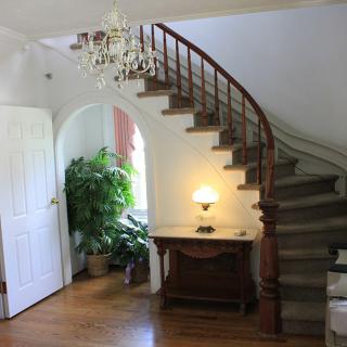 A cozy interior featuring a curved wooden staircase, a chandelier, and a well-lit corner with plants.