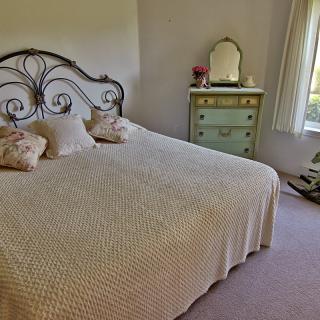 A cozy bedroom with an ornate iron headboard, a dresser with a mirror, and soft lighting through the window.