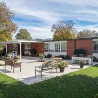 A modern house with a spacious patio and outdoor seating surrounded by a well-maintained lawn and trees under a blue sky.
