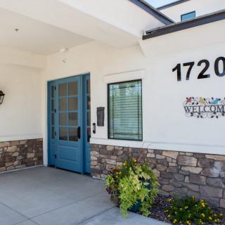 Front entrance of a building with a blue door and address number 1720 displayed on the wall, surrounded by stone accents and potted plants.
