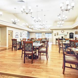 A spacious dining area with elegant chandeliers, wooden floors, and neatly arranged tables and chairs.