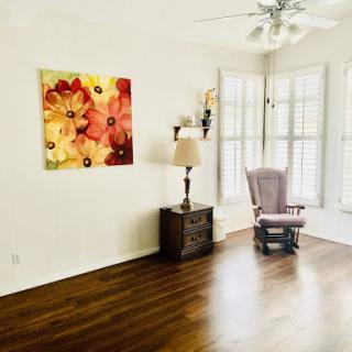 A cozy living room featuring floral wall art, a lamp, and a comfortable rocking chair.