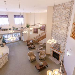 A spacious living room with a high ceiling, stone fireplace, and elegant chandeliers illuminating the seating area and staircase.