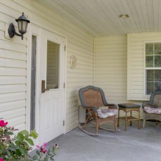 A cozy porch with two chairs and a small table, adorned with flowers and lit by a wall-mounted lamp.