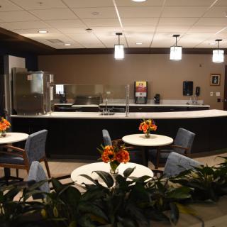 A modern cafe interior with tables and chairs, decorated with plants and floral arrangements.