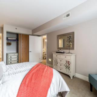 A cozy bedroom featuring a neatly made bed with a red throw, an open closet, and a decorative dresser with a mirror above it.