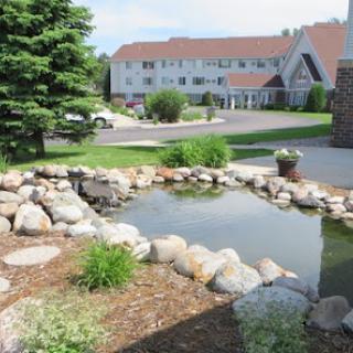A serene pond surrounded by rocks and greenery, with a hotel in the background.