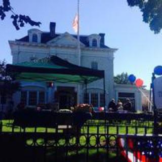 A historic building serves as the backdrop for an outdoor event, with colorful balloons and an American flag on display.