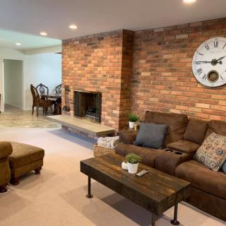 A cozy living room with a brick accent wall, featuring a fireplace, comfortable sofa, and stylish coffee table. The area opens up to a dining space.