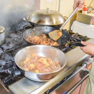Person cooking food in a kitchen using multiple pots and pans on a stove.