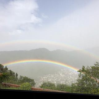 A stunning double rainbow arcs over a scenic landscape with mountains in the background.