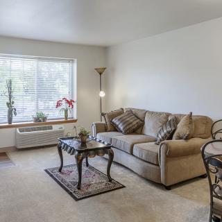 A cozy living room with a comfortable sofa, coffee table, and large window letting in natural light.