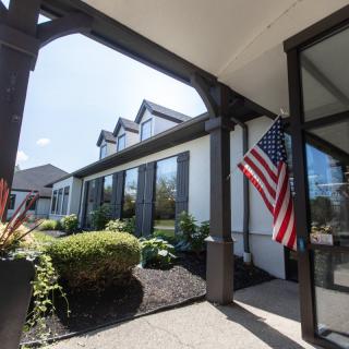 A modern house with a landscaped garden and an American flag displayed at the entrance on a sunny day.