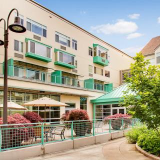 A modern apartment building with green accents and outdoor seating under patio umbrellas.