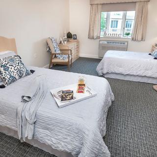 A cozy hotel room with two neatly made beds, a tray with food, and a window providing natural light.