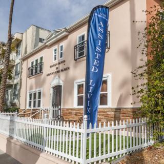 A residential building with a sign indicating 'Assisted Living' and a white picket fence in front.