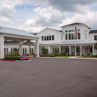 A large white building with a covered entrance and an American flag in front, set against a cloudy sky.