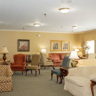 A cozy living room with a variety of chairs, sofas, artwork on the walls, and warm lighting.