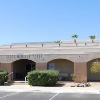 A modern commercial building with palm trees under a clear blue sky.