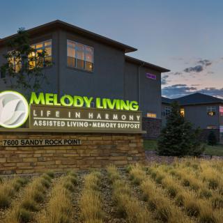 A view of the Melody Living assisted living facility with illuminated signage at dusk.