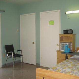 A simple room featuring a bed, a chair, and two doors.