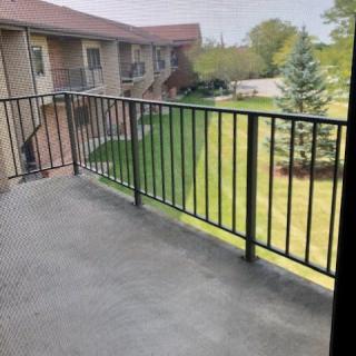 A view from a balcony overlooking a lawn and trees in a residential area.
