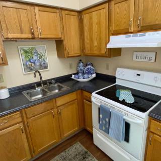 A cozy kitchen with wooden cabinets, an electric stove, and a sink, featuring a decorative tea set on the countertop.