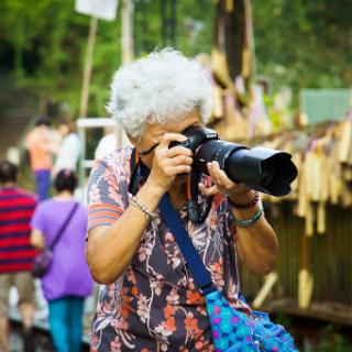 An elderly woman captures the moment with her camera at an outdoor event.