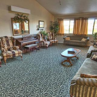 A spacious living room with patterned carpet, comfortable seating, and a piano.