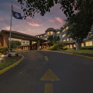 A building entrance at dusk with a flag and surrounding trees.