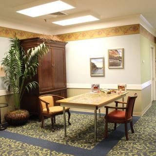 A cozy office space featuring a small meeting area with chairs and a table, accented by decorative elements such as a plant and framed artwork.