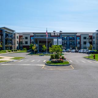 A modern apartment building with a landscaped parking lot and American flag.
