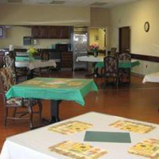 An empty dining room with tables and chairs set up, adjacent to a kitchen area.